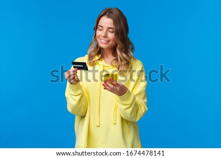 Young caucasian female with blond short hair using mobile phone and insert digit numbers of credit card to pay for her online purchase, shopping in internet store, smiling pleased