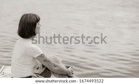Back view of young woman sitting on pier and using laptop