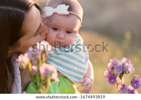 A mother and her baby daughter are enjoying flowers while out in nature.