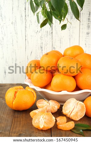 Ripe tangerines in bowl on table on wooden background