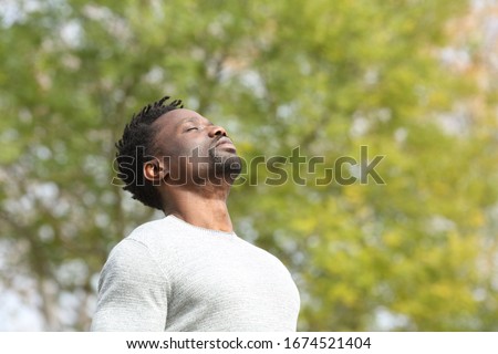 Black serious man breathing deeply fresh air in a park a sunny day with a green tree in the background Royalty-Free Stock Photo #1674521404