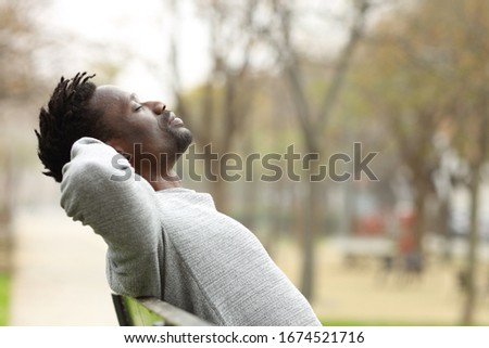 Side view portrait of a black man relaxing sitting on a bench in a park Royalty-Free Stock Photo #1674521716