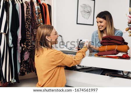 Beautiful young woman paying her new clothes buyed in expensive boutique with credit card.