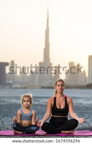 Beautiful young woman and her little daughter doing yoga together at sunset in Dubai. With city view. Skyline Dubai