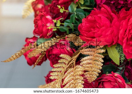 Close up shot of a fake golden pine leaf with a beautiful red bouquet of flowers.