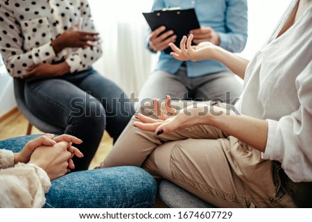 Unrecognizable vulnerable woman participates in group therapy session. Unrecognizable Caucasian person gestures while speaking. Group of people sitting in a circle during therapy.  Royalty-Free Stock Photo #1674607729