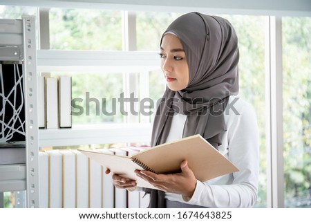 Asian Muslim businesswoman choosing a books on book shelf in her office, Muslim woman student.