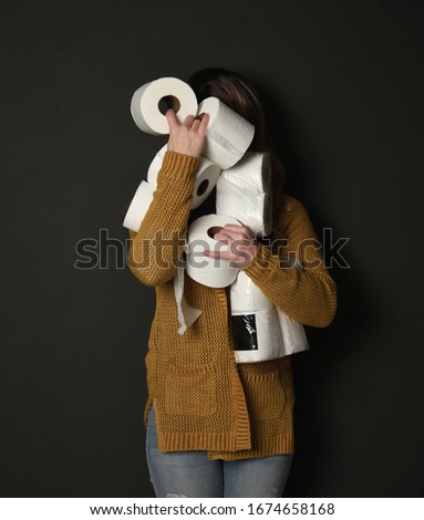 A woman is holding a stock pile of toilet paper supplies for a consumer demand concept regarding the corona virus pandemic.
