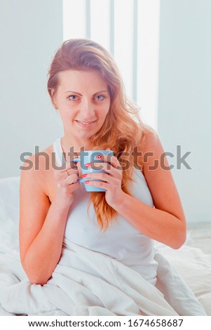 Good morning and good mood starts with a delicious morning coffee.  Young beautiful woman sitting on bed holding a cup of coffee. Vertical image.
