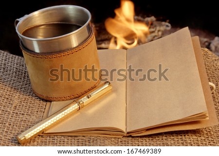 Old Notebook, Golden fountain Pen, and a Mug of Coffee in front of the Campfire