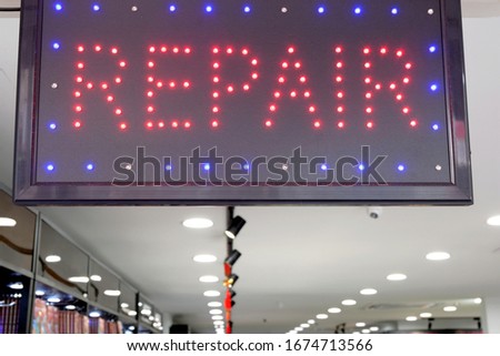 Illuminated repair signage lighted with LEDs hanging in front of an electronic shop. A store offering repair and maintenance services, such as fixing customers' mobile phones, pcs and other gadgets.