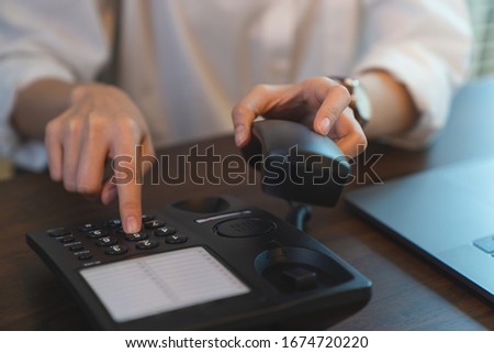 Hand press the phone button on the office desk.