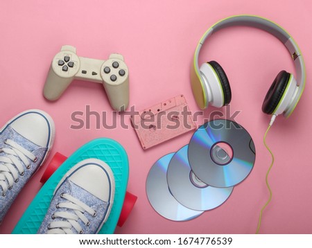 Flat lay hipster composition. Cruiser board, stereo headphones, audio cassette, cd discs, gamepad
 on pink background. Retro 80s entertainments. Top view