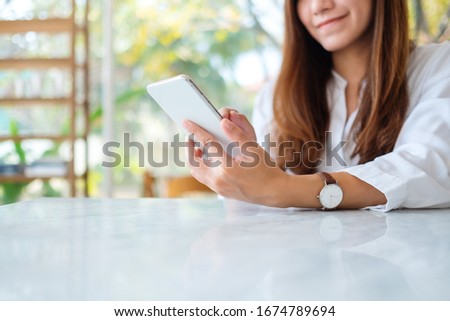 Closeup image of a beautiful asian woman holding and using mobile phone in cafe