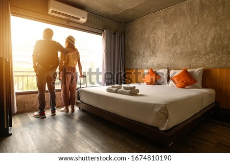 Portrait of young couple tourist standing nearly window, looking to beautiful view outside in hotel/resort bedroom after check-in. Conceptual of couple travel and vacation in their honeymoon period. Royalty-Free Stock Photo #1674810190