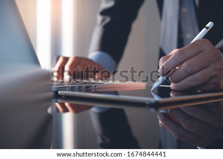 Businessman using stylus pen signing contract on digital tablet working on laptop computer in modern office, electronic signature. Business man taking note on touchpad, business and technology concept