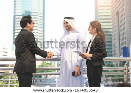 

A business meeting with an arab man and his assistance or a translator, shaking each other’s hands in greetings and introduction, discussing and planning within the urban city district as background