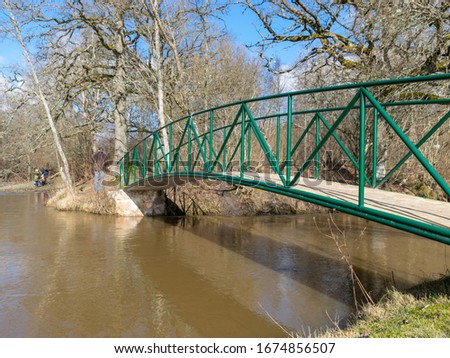spring landscape with river and bare trees on river bank, green bridge over river, Abava river, Latvia