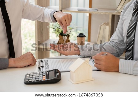 Real estate agent broker hand over the house key to the new owner after completing the signing according to agreement renting a house and buy house insurance Home insurance concept.