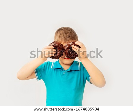 Little happy cute boy is eating donut on white background wall. child is having fun with donut. Tasty food for kids. Funny time at home with sweet food. 
