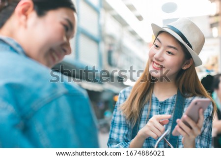 Young Asian female friends taking her vacation and eating street food  In Bangkok. asian woman relax and talking with happiness emotion.She shoot photo by mobile phone with friend.