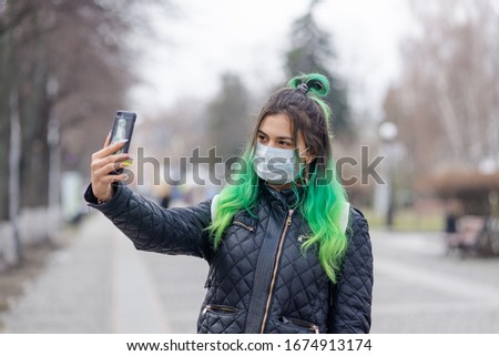 Young woman with green hair in a medical mask takes a selfie on the street of a European city.