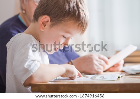 little boy 4 years old reading book. He is sitting on chair  in sunny living room watching pictures in story. Kid doing homework for elementary school or kindergarten. Children study.