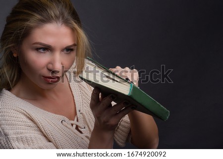 Portrait of a middle aged blonde woman in white clothes on a light gray background. he look in half-open book. concept of adult education