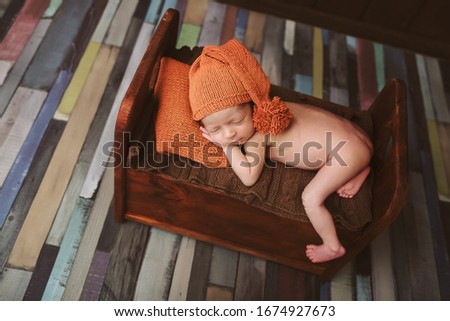 Cute newborn baby in hat on a brown bed and orange pillow . Sleeping baby on a dark background. Closeup portrait of newborn baby. Baby goods packing template. Nursery. Medical and healthy concept.
