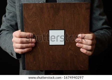 Smiling Man holds Photobooks in a wooden cover on dark background. Copy space