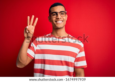 Young handsome african american man wearing casual striped t-shirt and glasses showing and pointing up with fingers number three while smiling confident and happy.