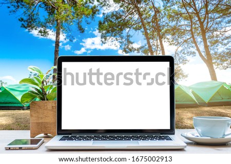 Mockup of laptop computer with empty screen with coffee cup and smartphone on table in forest summer camp among meadow on Mountain,recreation and Tourist holiday outdoor concept