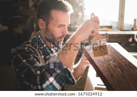 Craftsman painting a wooden board by paintbrush in his carpentry workshop
