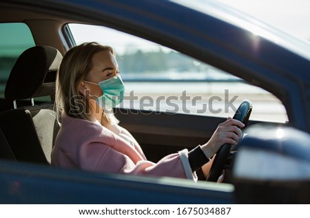 Woman in protective mask driving a car on road. Safe traveling. Royalty-Free Stock Photo #1675034887