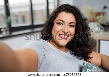 people, technology and leisure concept - happy smiling young woman taking selfie at home
