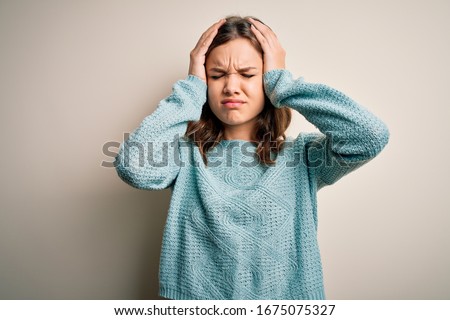 Young blonde girl wearing casual blue winter sweater over isolated background suffering from headache desperate and stressed because pain and migraine. Hands on head. Royalty-Free Stock Photo #1675075327