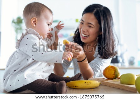 Shot of happy young mother feeding her cute baby girl with a banana in the kitchen at home. Royalty-Free Stock Photo #1675075765