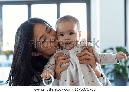Shot of pretty young mother kissing her little daughter while she looks at the camera at home.