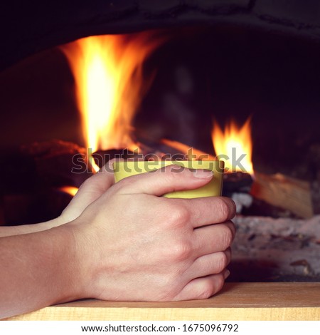 hands are holding a yellow cup on the background of the fireplace. warming atmosphere for recovery