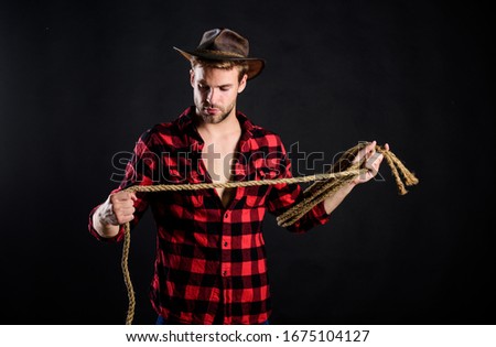 Lasso is used in rodeos as part of competitive events. Lasso can be tied or wrapped. Western life. Man unshaven cowboy black background. Man wearing hat hold rope. Lasso tool of American cowboy.