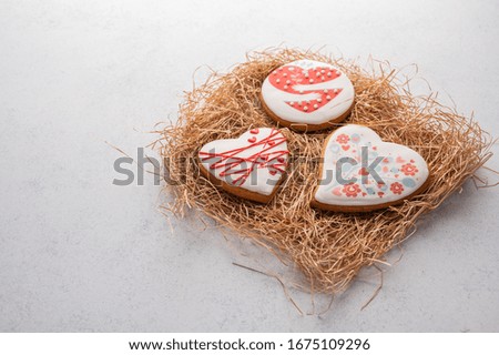 Gingerbread with heart-shaped glaze on a straw substrate on a grey textured background
