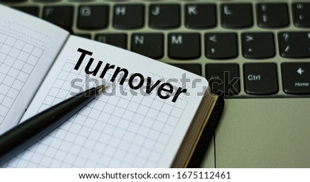 notebook with a pen and the word TURNOVER , on the background of a laptop