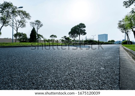 Asphalt road leading to a city with tall buildings through green meadow