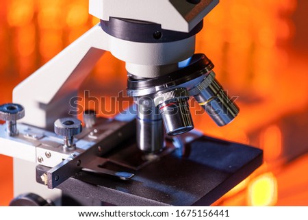 Close up of microscope lenses focused on a specimen in warm orange light light. Laboratory flask in the background. Royalty-Free Stock Photo #1675156441