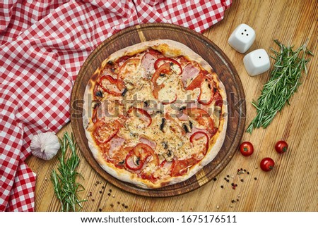 Pizza with ham, bell pepper, mushrooms, tomatoes, cheese and white sauce on a wooden tray. Pizza in composition with ingredients on a wooden table