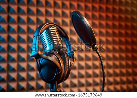 Retro microphone with professional headphones with pop filter for singing or recording a podcast on acoustic foam panel background, colorful light