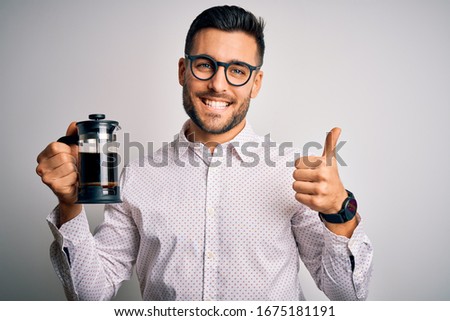 Young handsome man making coffee using french press coffeemaker over isolated background happy with big smile doing ok sign, thumb up with fingers, excellent sign