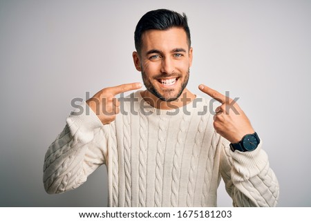 Young handsome man wearing casual sweater standing over isolated white background smiling cheerful showing and pointing with fingers teeth and mouth. Dental health concept. Royalty-Free Stock Photo #1675181203