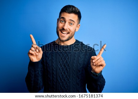 Young handsome man wearing casual sweater standing over isolated blue background smiling confident pointing with fingers to different directions. Copy space for advertisement