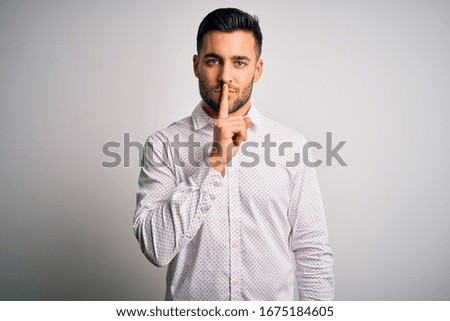 Young handsome man wearing elegant shirt standing over isolated white background asking to be quiet with finger on lips. Silence and secret concept.